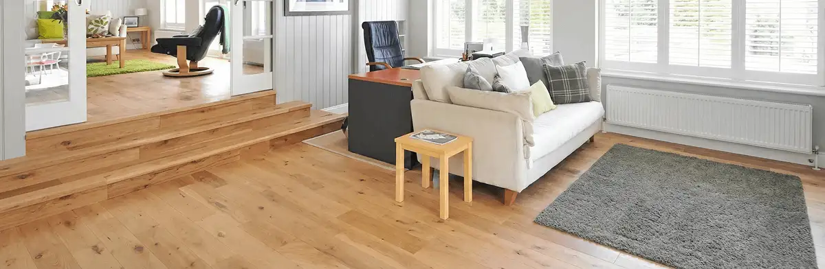 A modern living room with professionally installed laminate flooring, a beige sofa, a small side table, a gray rug, and large windows with white shutters in Louisville, KY